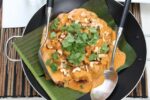 chicken tikka masala in a wok on top of banana leaves with a large spoon