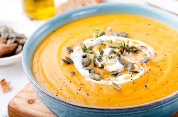 A blue bowl of miso butternut squash soup topped with pumpkin seeds and creme fraiche on top of a wooden board.