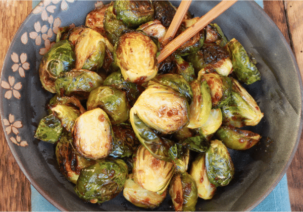 roasted Brussels sprouts in an Asian sauce on a gray bowl
