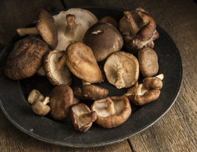 a bowl of fresh shiitake mushrooms on a wooden board