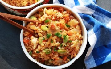 a bowl of cauliflower kimchi fried rice with chopsticks and a blue and white napkin on the side