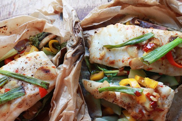 Chilean sea bass filets cooked in parchment paper with colorful vegetables on top.