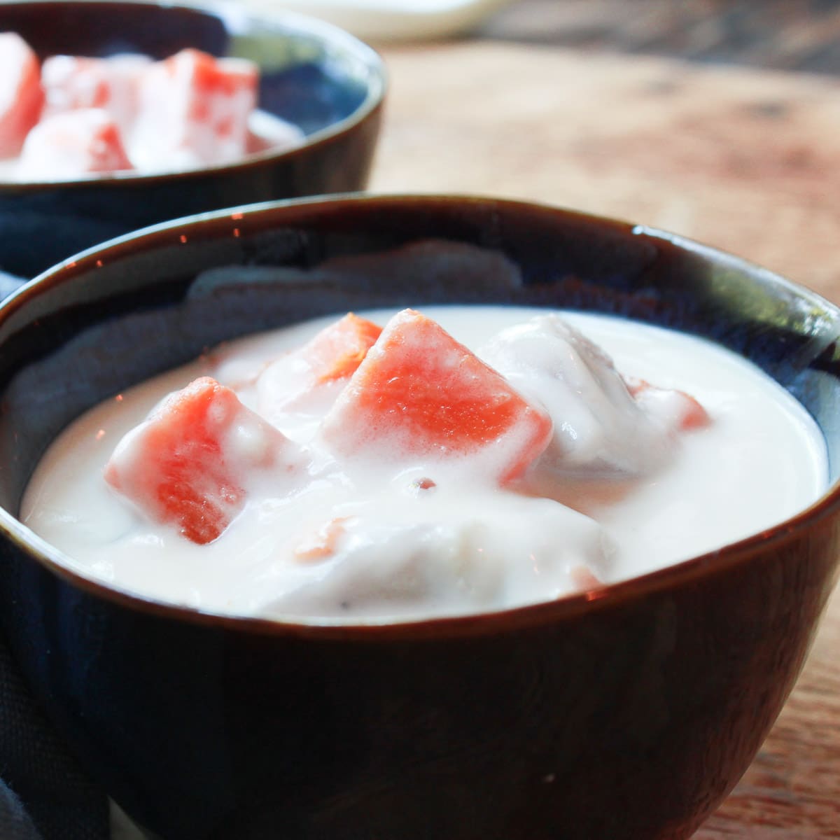 Two dark bowls filled with coconut dessert soup with sweet potatoes on top of a wooden board and a blue napkin on the side.