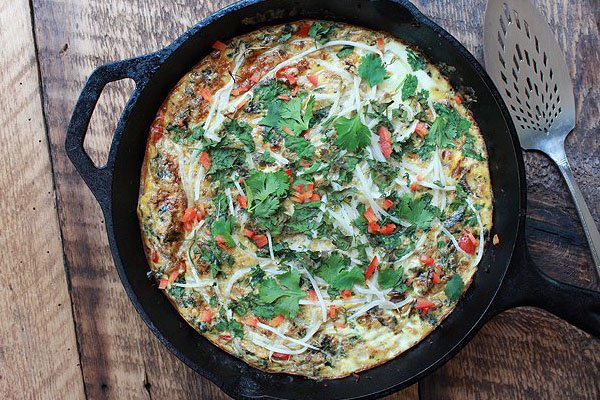 A cooked vegetarian frittata inside a cast iron skillet topped with peppers and cilantro.