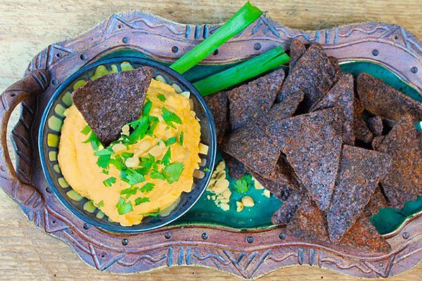 butternut squash dip in a bowl on top of a platter with black tortilla chips on the side