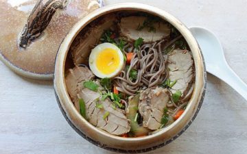 Pork soup with soba noodles in a dark soup bowl topped with a soft boiled egg.
