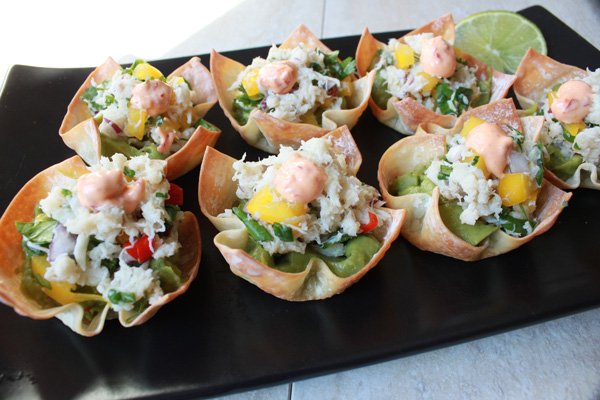spicy crab salad on top of guacamole inside a baked wonton cup on a black plate
