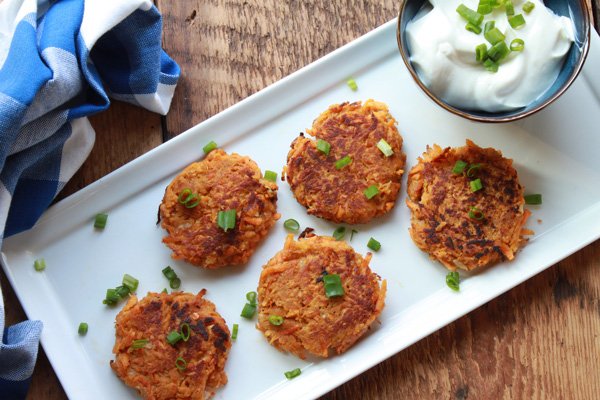 Five-spice Asian latkes placed on a narrow white serving platter with a side of sour cream place on top of a wooden board.