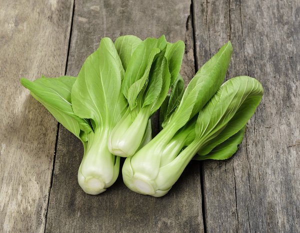 Three bunches of vibrant green baby bok choy on top of a dark wooden plank surface.