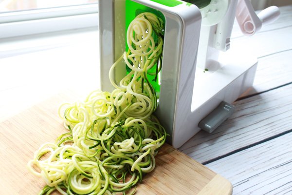 Zucchini being spiralized into noodles on top of a wooden board.