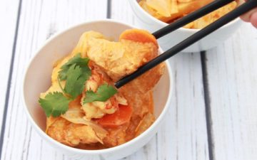 a white bowl filled with coconut curry tofu and shrimp on a white board with chopsticks