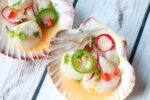 Spicy scallop ceviche presented in pretty shell bowls placed on top of a white wooden board.