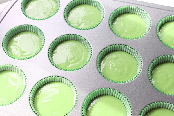 A cupcake tray filled with uncooked matcha green tea batter ready for baking in the oven.