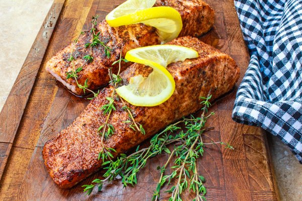 seared salmon filets topped with fresh herbs and a lemon slice on a wooden cutting board