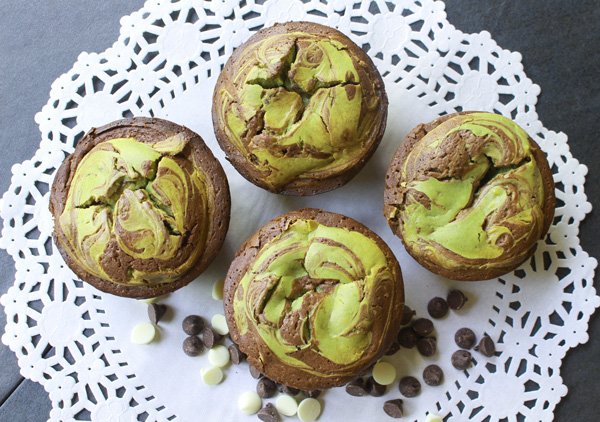 Four matcha cheesecake muffins on a white doily with chocolate chips on the side.