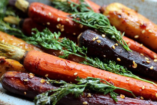Close up shot of colorful roasted rainbow carrots with tops on   garnished with sesame seeds.