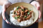 Instant Pot Korean Inspired Pulled Pork over rice being held in a beige bowl garnished with sliced green onions