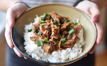 Instant Pot Korean Inspired Pulled Pork over rice being held in a beige bowl garnished with sliced green onions