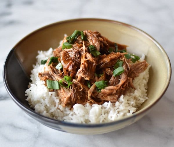 Instant Pot Korean Inspired Pulled Pork over white rice in a beige bowl garnished with sliced green onions.