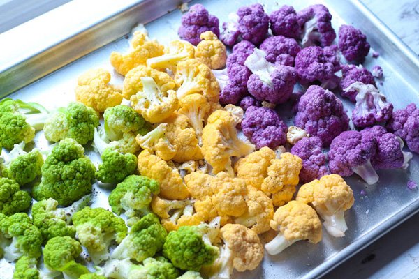 Chopped purple, orange and green cauliflower florets on a sheet pan ready for the oven.