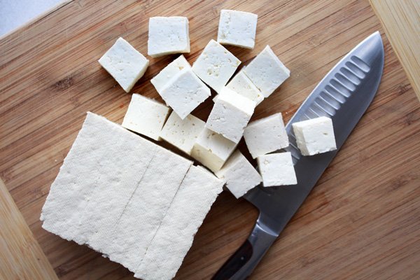 Tofu cubes on a wooden cutting board with a chef's knife