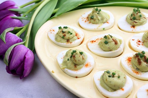 avocado deviled eggs in an egg tray with purple tulips along side