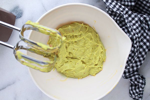 hand blender beating avocado deviled eggs mixture in a white mixing bowl
