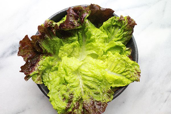 Pieces of lettuce leave in a black bowl on top of a marble surface.
