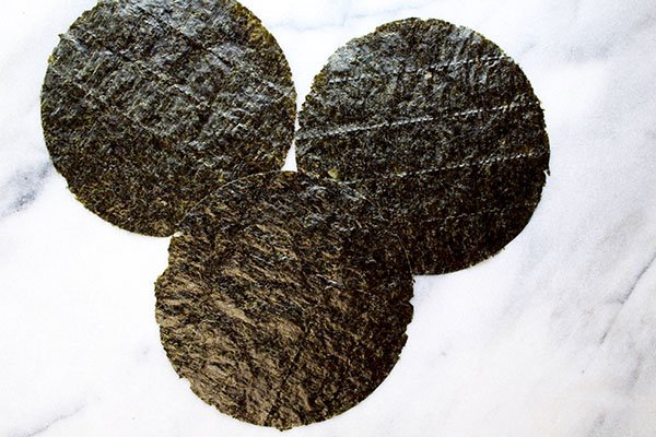 Three circular nori seaweed sheets placed on top of a marble surface.