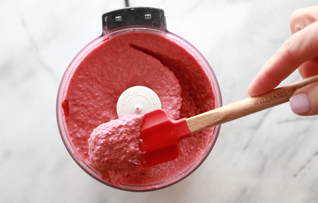 red beet hummus pureed in a small food processor with a red rubber spatula