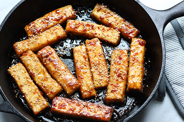 Crispy tofu strips being browned in a black cast iron skillet with an oven mitt on the side