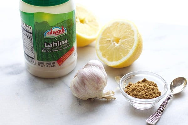 tahini tahina in a jar with lemons, garlic, and a bowl of cumin on the side with a small silver spoon