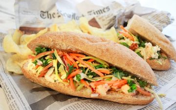 A lobster banh mi sandwich on top of a newspaper with potato chips on the side.