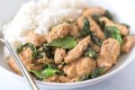 Thai basil chicken topped with green herbs in a white bowl with a side of steamed white rice.
