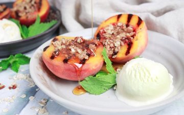 grilled peaches topped with a five spice oats crumble and a side of vanilla ice cream on a white plate