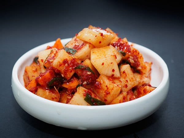 A white bowl filled with Korean Kimchi on top of a black surface.