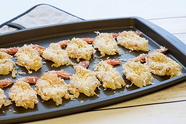 A baking tray layered with jumbo coconut shrimp ready for the oven, on top of a white wooden board.