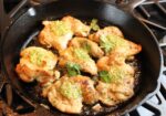 Lemongrass chicken thighs cooking in a cast iron pan topped with fresh cilantro.