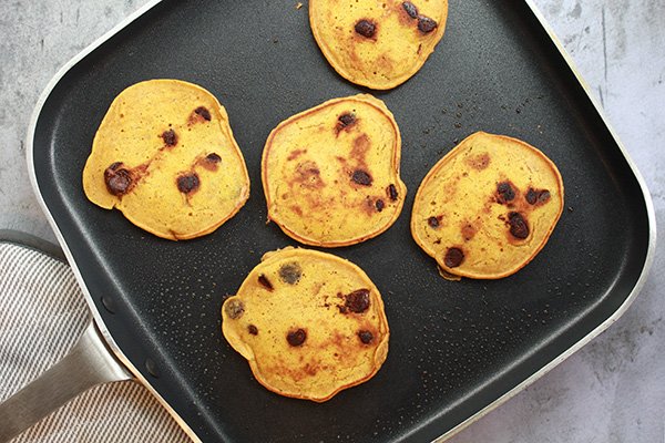 Pumpkin chocolate chip pancakes cooked on a stove-top griddle place on top of a marble surface.