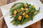 A white plate topped with cooked curry green beans and cubes of tofu sprinkled with chopped Thai chili peppers.