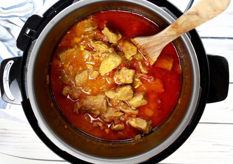 Pieces of cooked pork covered with sauce inside the Instant Pot with a wooden spatula inserted.