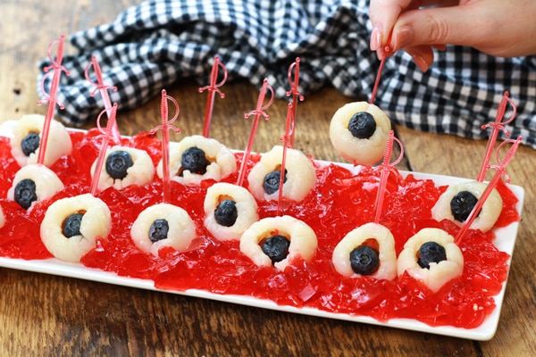 A white tray with lychee eyeballs on top of strawberry jello