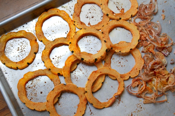 Rings of roasted delicata squash on top of a baking sheet with roasted shallots on the side.