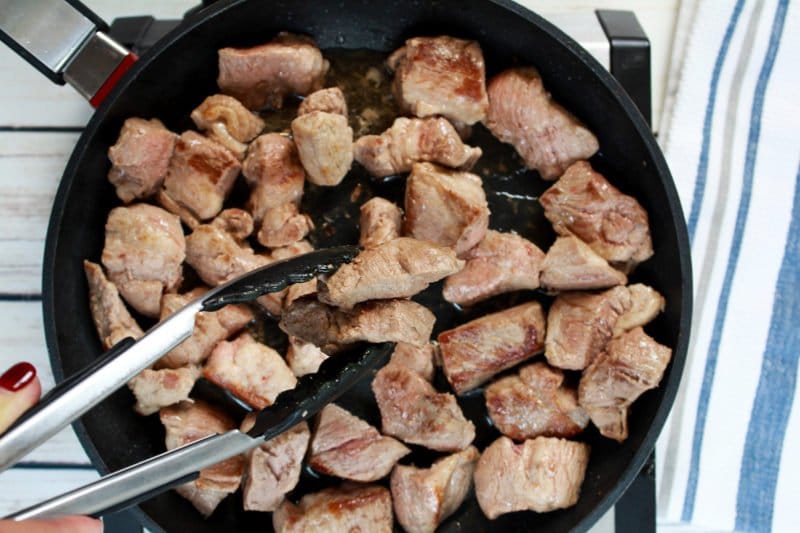seared pork butt pieces being seared in a cast iron pan