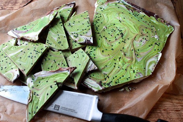 vibrant green matcha holiday bark topped with black sesame seeds on top of parchment paper with a chef's knife on the side