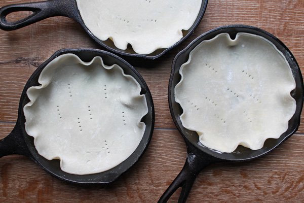 Three mini cast iron skillets with raw pastry lined inside on top of a wooden board.