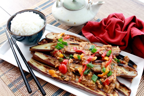 Roasted Chinese eggplant strips on a white plate topped with a garlic and pepper sauce.