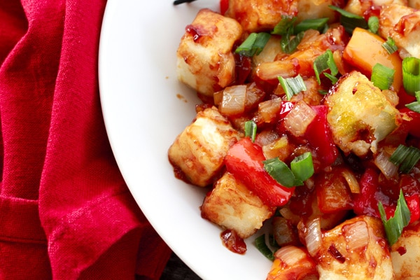 Crispy tofu cubes in a sweet and sour sauce in a white bowl with a red napkin on the side.