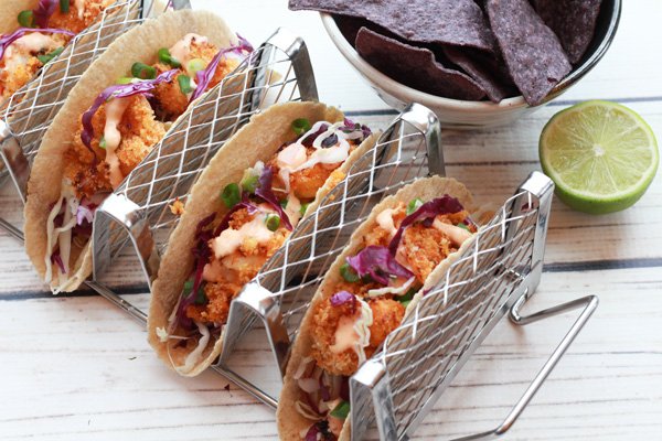 bang bang shrimp tacos in a taco holder with chips and a lime on the side.