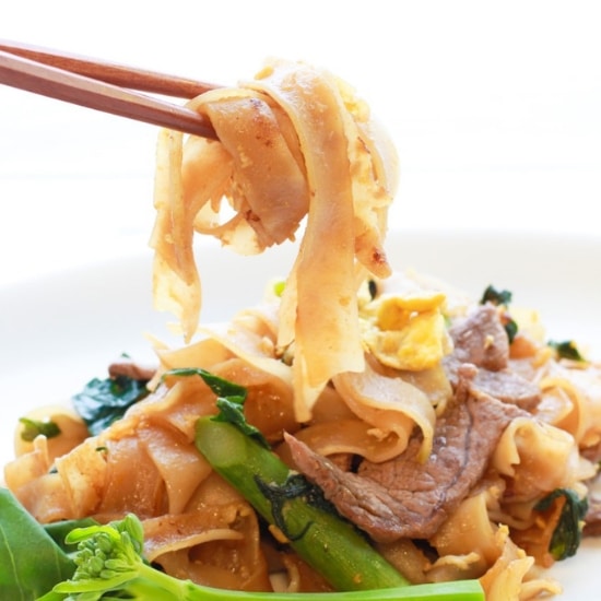 Thai Pad See Ew stir fried noodles on a plate with chopsticks and Chinese broccoli.